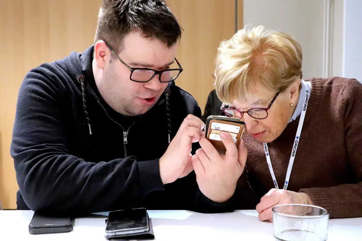 Man och kvinna tittar på en telefon. Kvinnan använder en förstoringsglasfunktion på telefonen, en hjälp för synskadade.