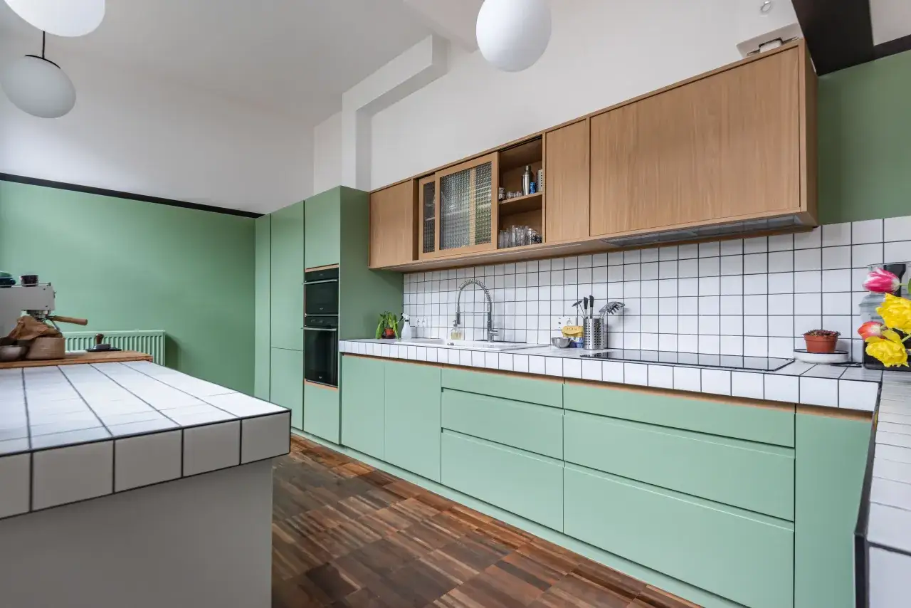 Plan de travail cuisine carrelage blanc et vert menthe, avec placards en bois et sol en parquet.