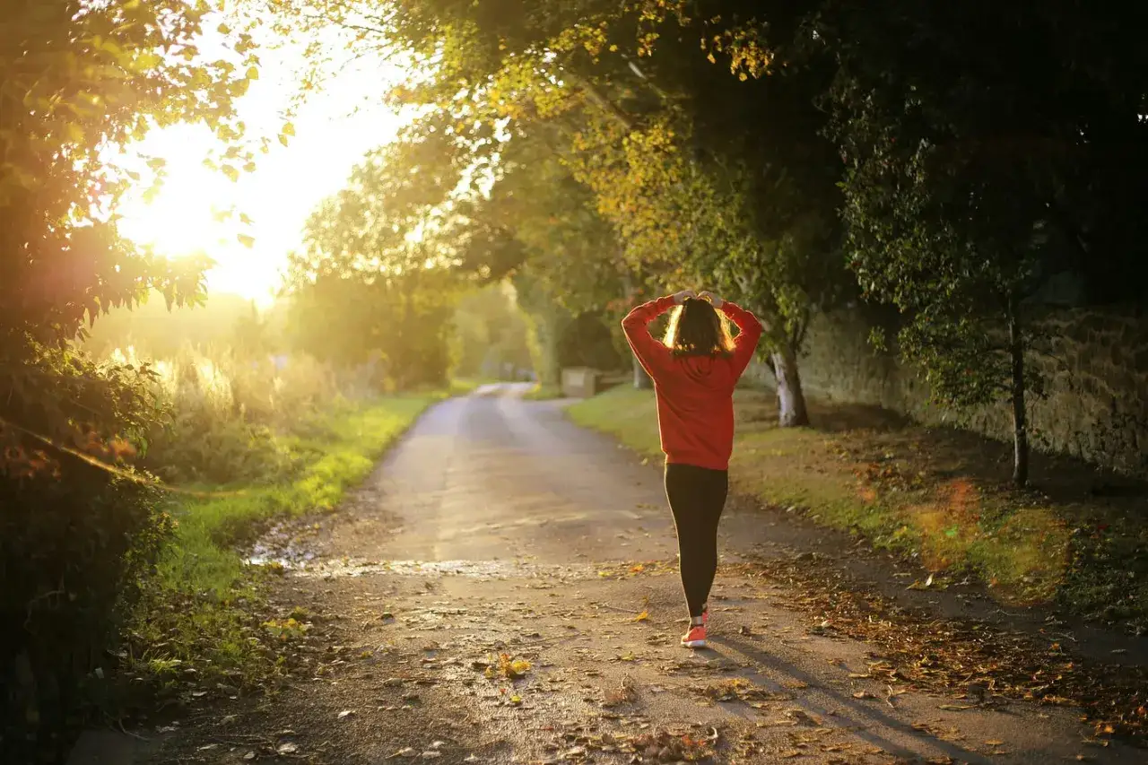 Frau im roten Hoodie joggt auf einem sonnigen Weg. Sie fragt sich, ob joggen gesund ist.