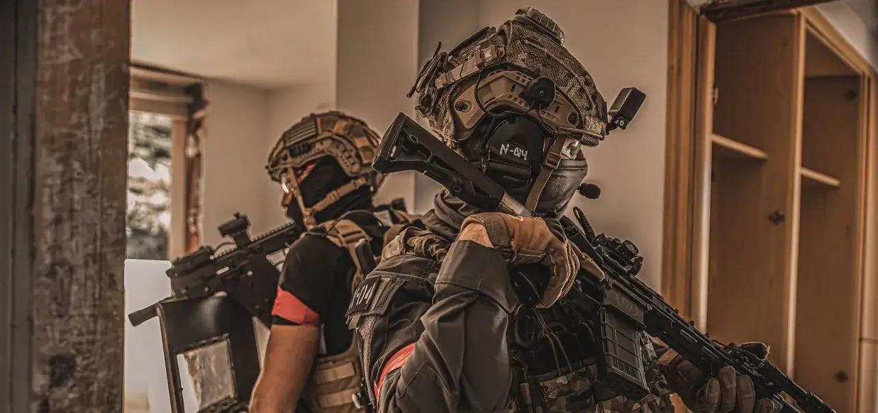 Dos jugadores de **deporte airsoft** con equipo t&aacute;ctico y r&eacute;plicas de armas se preparan para la acci&oacute;n en un entorno interior.