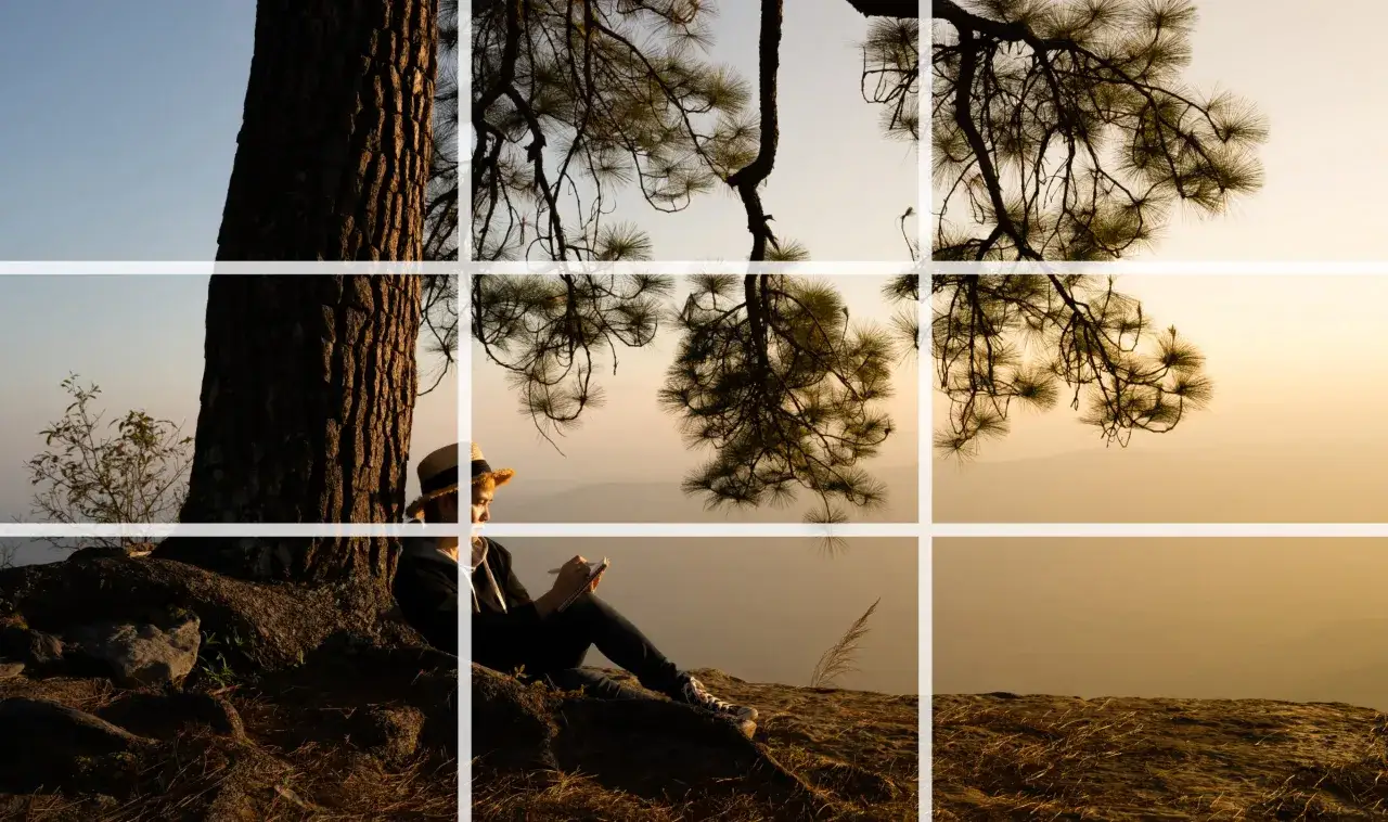 Une jeune femme au chapeau de paille écrit dans un carnet, adossée à un arbre. La lumière dorée du coucher de soleil baigne la scène, une belle **technique photo** de composition.