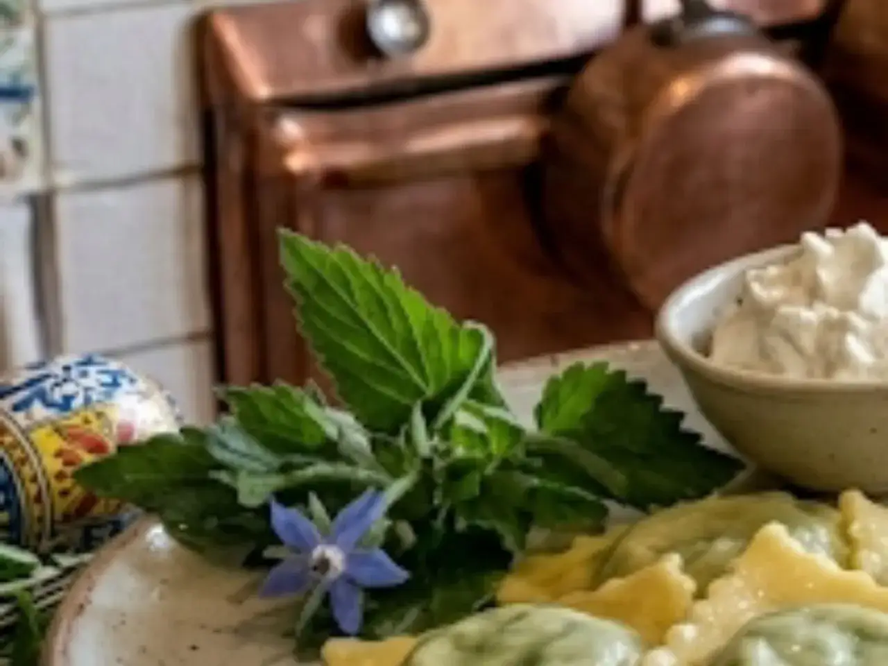 Ravioli di borragine freschi, guarniti con un fiore di borragine e accompagnati da una ciotolina di formaggio cremoso.