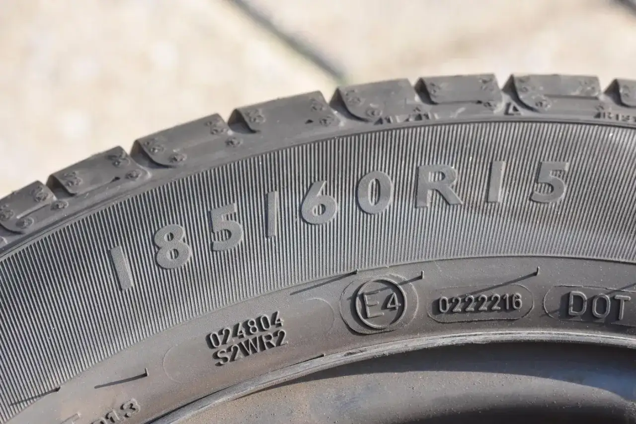 Widok z bliska na oponę z oznaczeniem 185/60R15. Widać niewielką czerwoną kropkę na boku opony, która może wskazywać na punkt równowagi.
