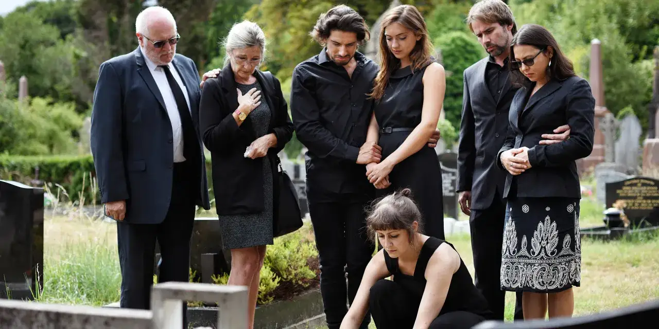 Trauernde Familie auf einem Friedhof. Mögliche Nachteile beim Kirchenaustritt könnten hier die fehlende kirchliche Beerdigung sein.