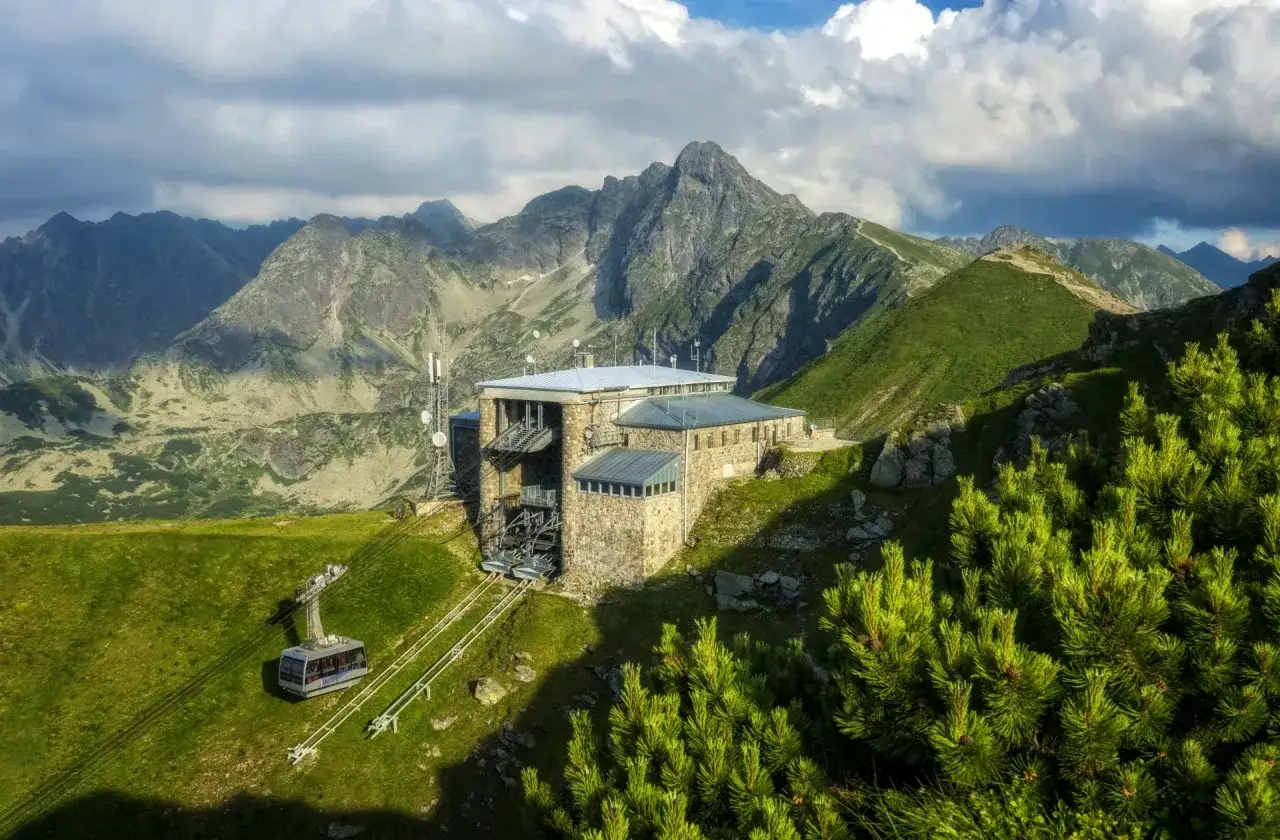 Górna stacja kolejki na Kasprowy Wierch z kamiennym budynkiem i widokiem na Tatry. Kolejka zjeżdża po zboczu.