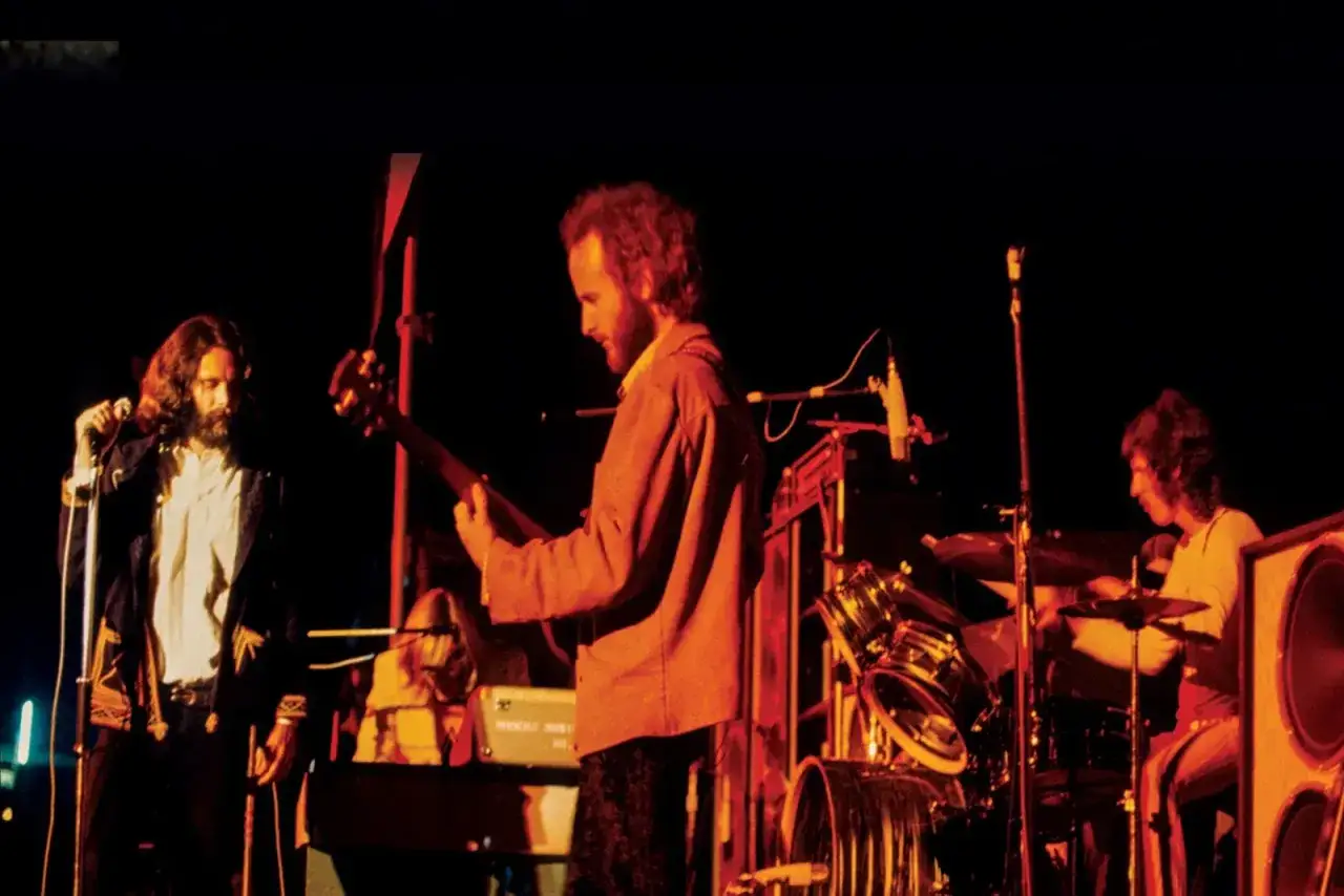 Jim Morrison singt, w&auml;hrend andere Mitglieder von The Doors auf der B&uuml;hne spielen. Ein Bassist und ein Schlagzeuger sind zu sehen.