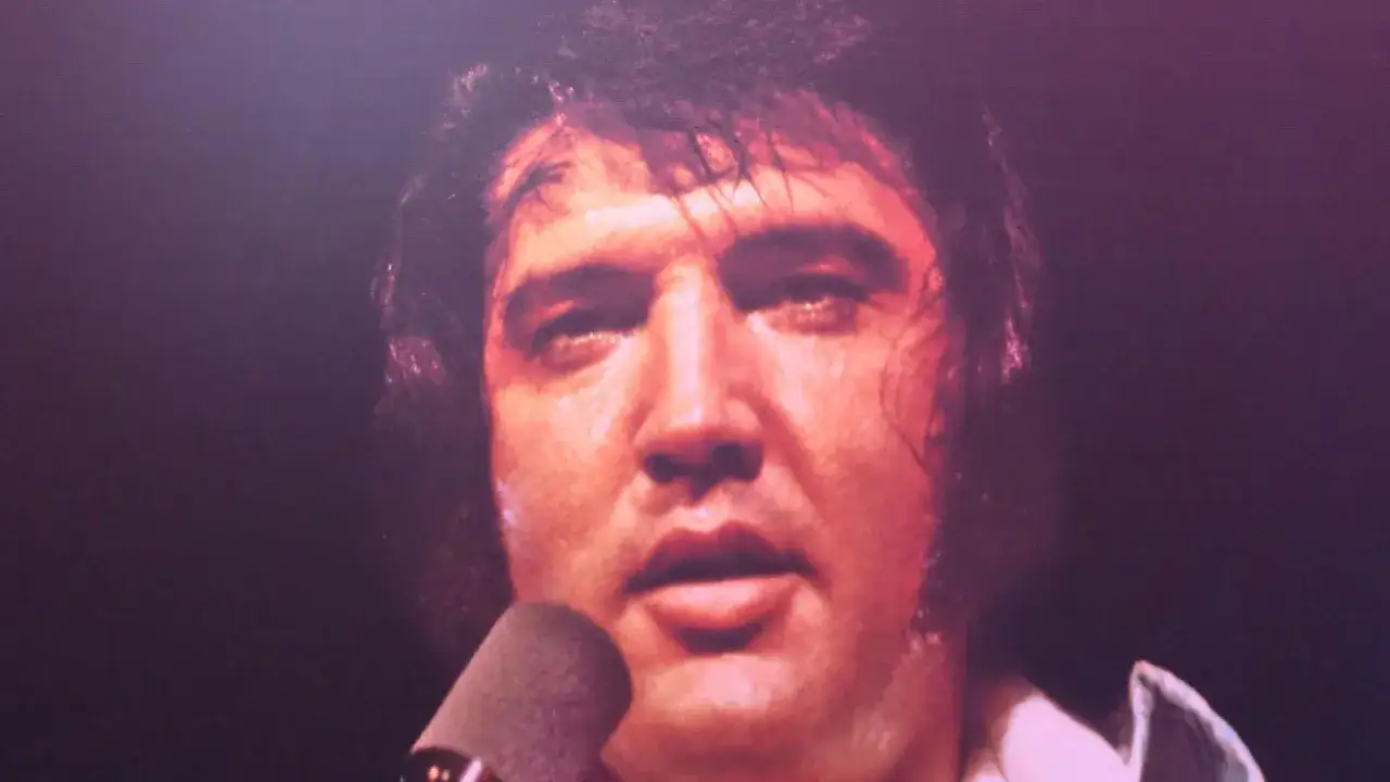 Elvis Presley, sichtlich ersch&ouml;pft, singt in ein Mikrofon. Ein Moment, der an seinen elvis presley last concert erinnert.