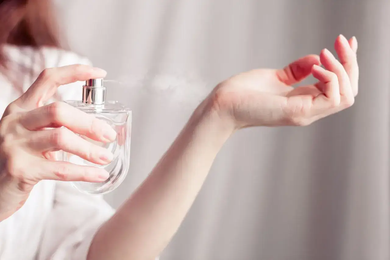Kobieta aplikująca perfumy na sk&oacute;rę, podkreślając punkty tętna