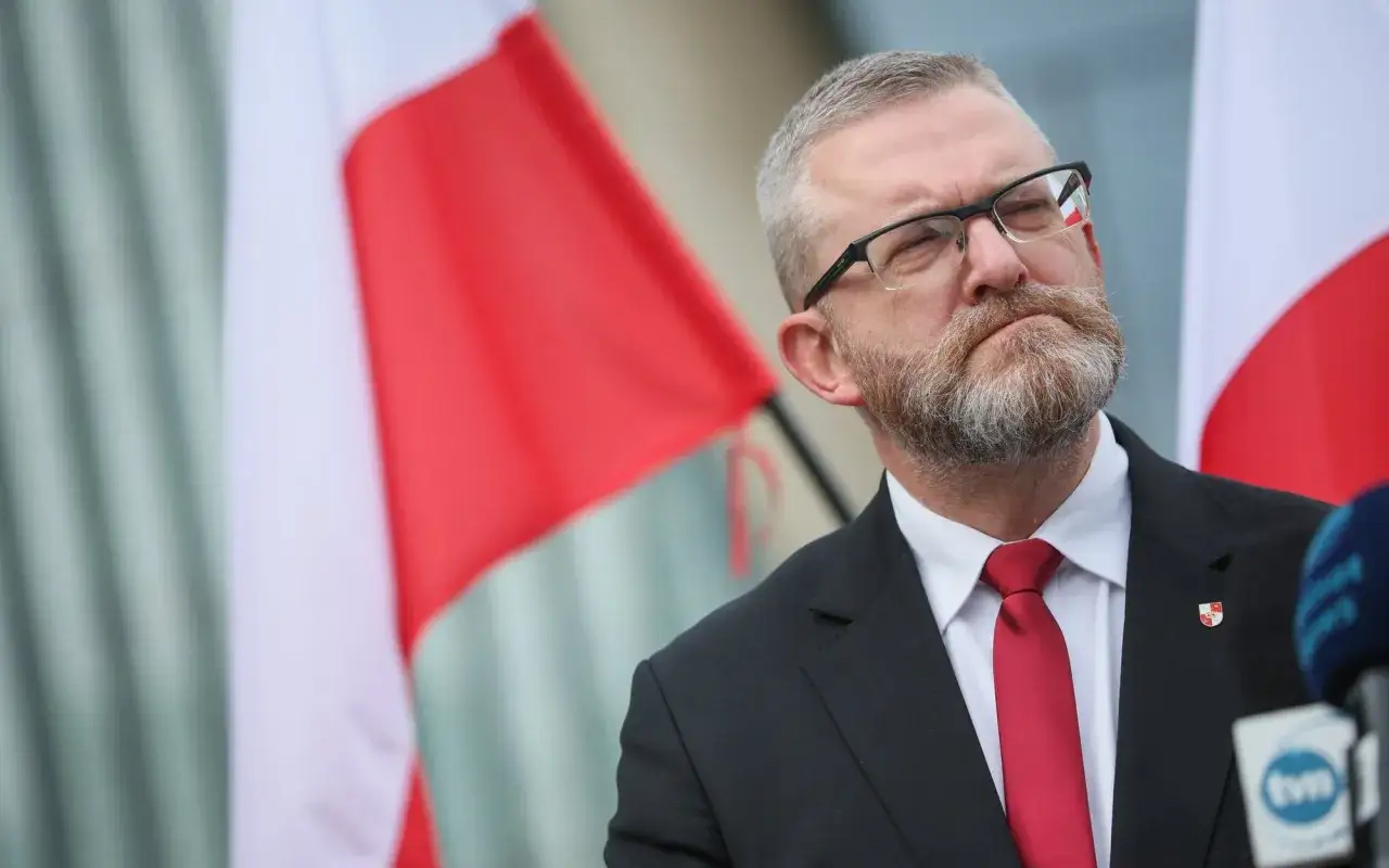 Mężczyzna w garniturze i czerwonym krawacie, na tle polskich flag. Czy Konfederacja Korony Polskiej planuje samodzielny start w wyborach?
