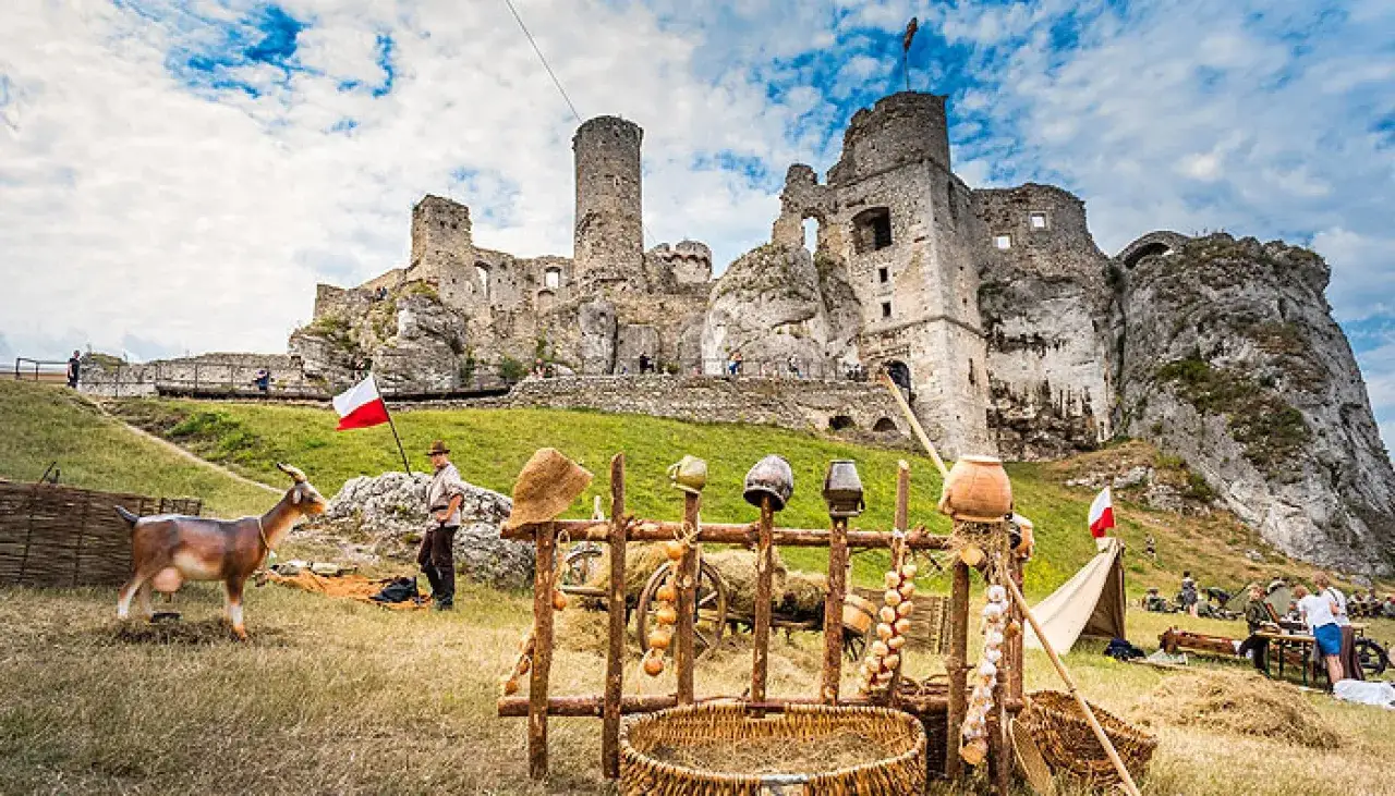Zamek w Ogrodzieńcu, malownicza ruina na skale, z kozą i polską flagą. Scena jak z historycznego jarmarku.