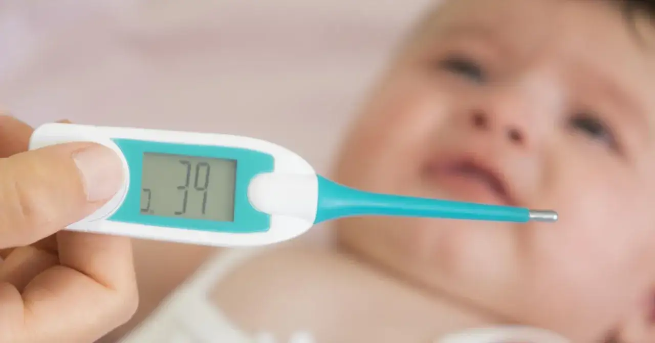 Cyfrowy termometr pokazuje 39 stopni. Zaniepokojona mama mierzy temperaturę niemowlaka.