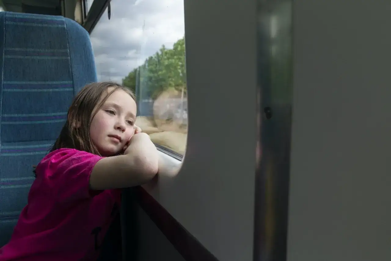 Dziewczynka wpatruje się przez okno pociągu. Zastanawia się, od ilu lat można jeździć samemu pociągiem.