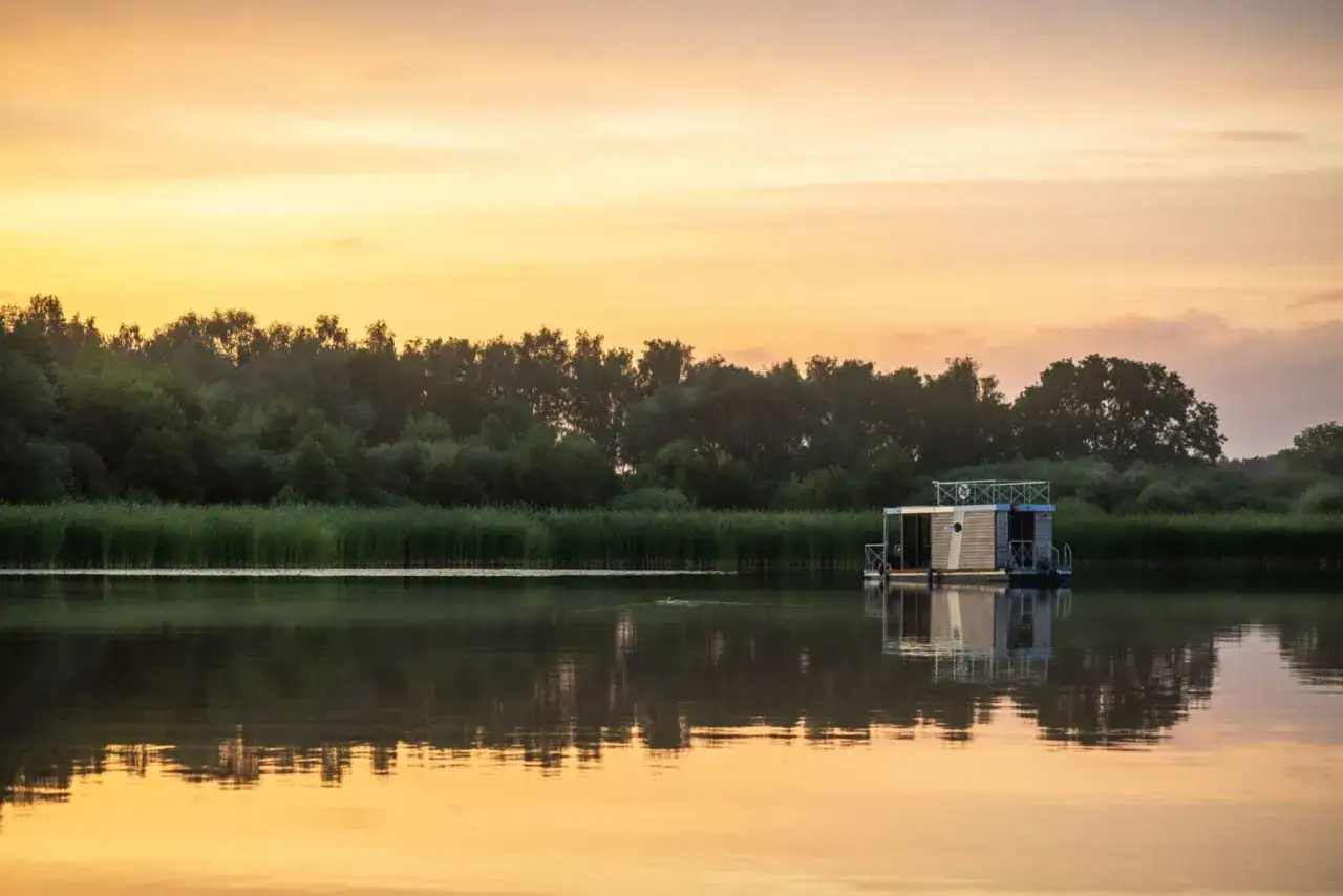 Ein Hausboot treibt friedlich auf dem Plauer See im warmen Licht des Sonnenuntergangs.