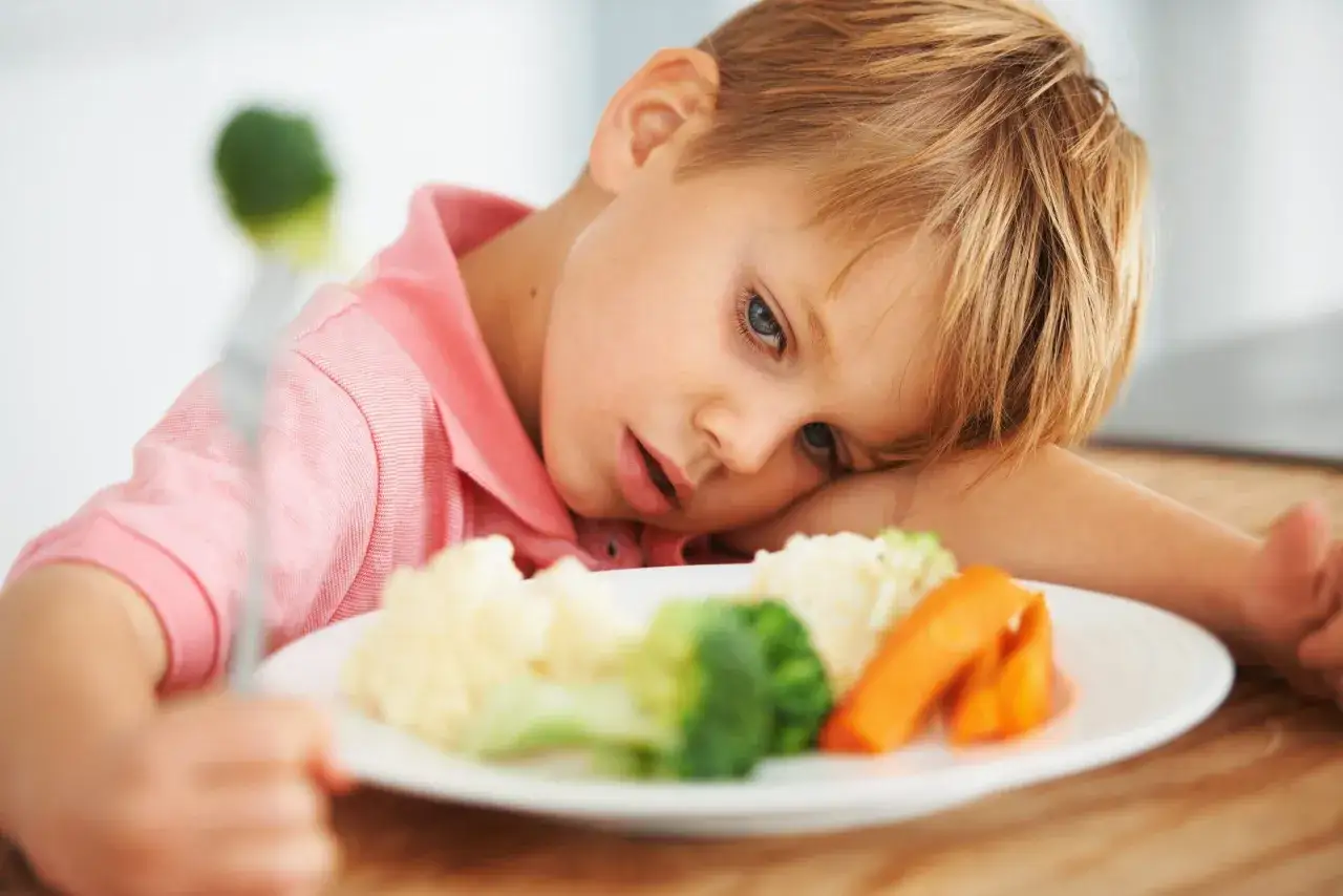 Jongetje met autisme kijkt lusteloos naar groenten op zijn bord. Eten kan een uitdaging zijn.
