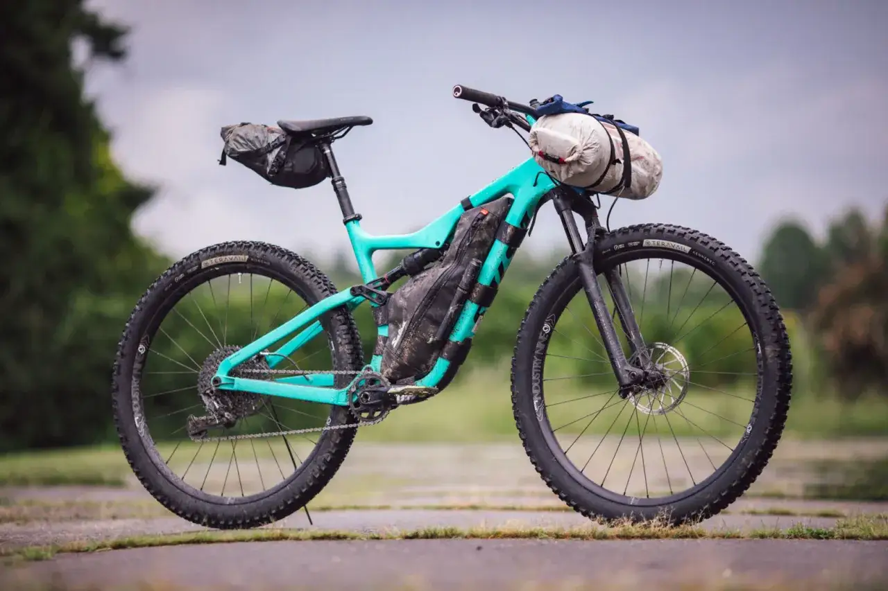 Turkusowy rower górski gotowy na bike packing, z sakwami pod siodełkiem, na ramie i kierownicy.