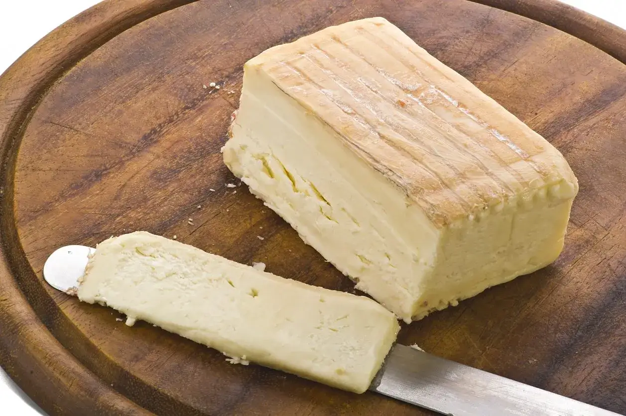 Un pezzo di taleggio con la sua crosta leggermente muffa, pronto per essere affettato su un tagliere di legno.