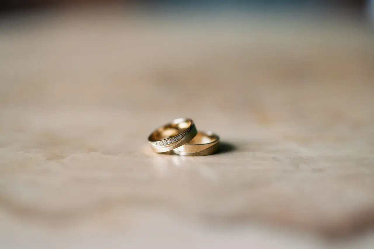 Dwa złote obrączki ślubne, jedna z brylantami, leżą obok siebie. Symbolizują miłość i wierność, a ich blask przypomina o pięknych przesądach ślubnych.