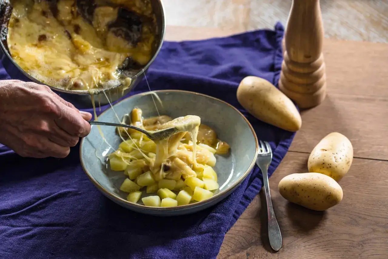 Une cuillère sert du fromage fondu sur des pommes de terre coupées en dés. Une recette de matouille réconfortante.