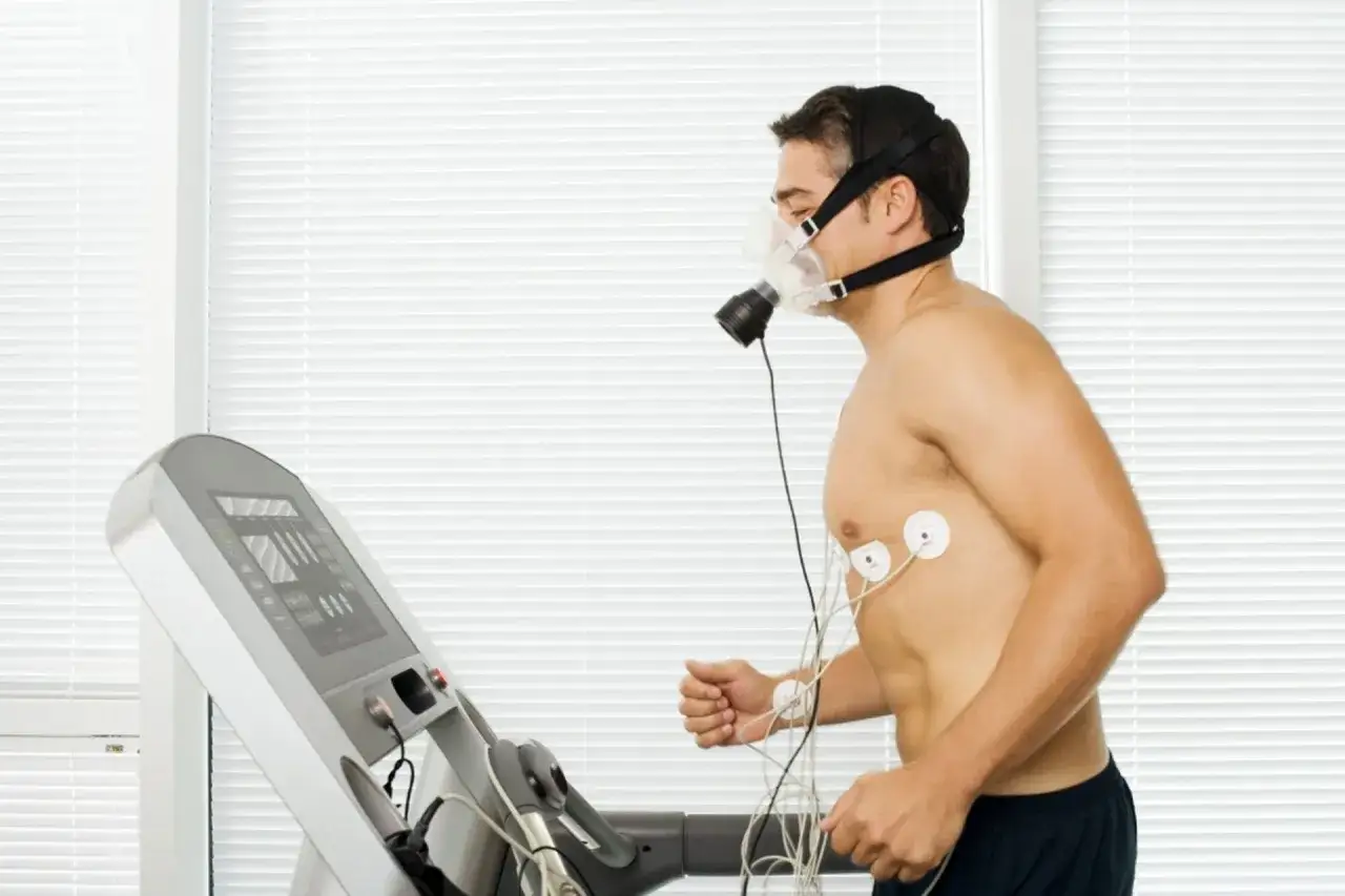 Mężczyzna w masce tlenowej biegnie na bieżni, podłączony do EKG. Badanie wydolnościowe określa pułap tlenowy normy.