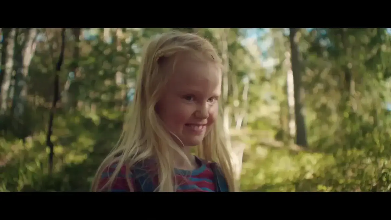 Ett leende barn med blont hår i en skog. Trots sitt utseende av de oskyldiga, anas en hemlighet i blicken.