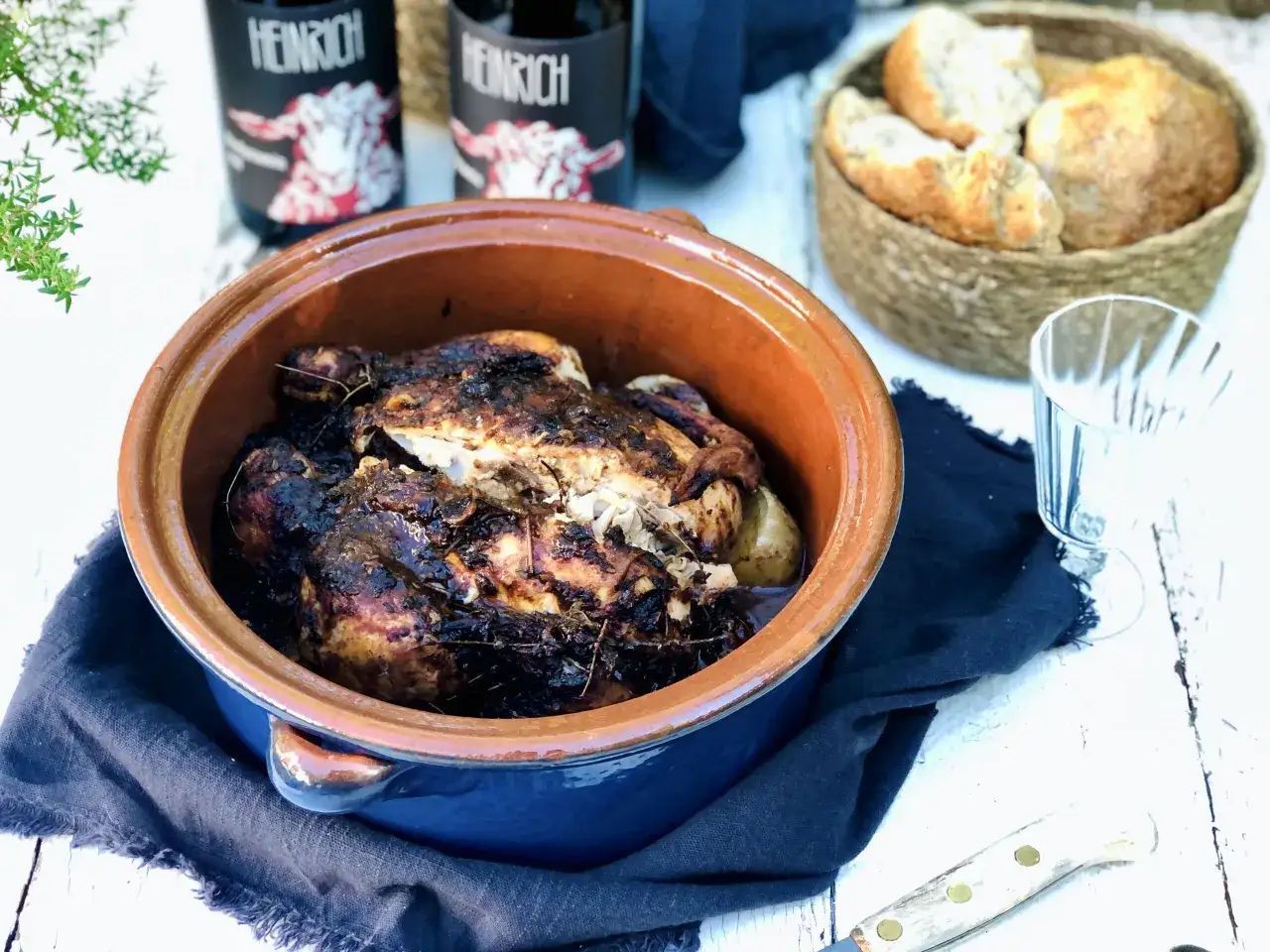En saftig kyckling i lergryta, perfekt tillagad med örter. Bredvid syns nybakat bröd och flaskor från Heinrich.