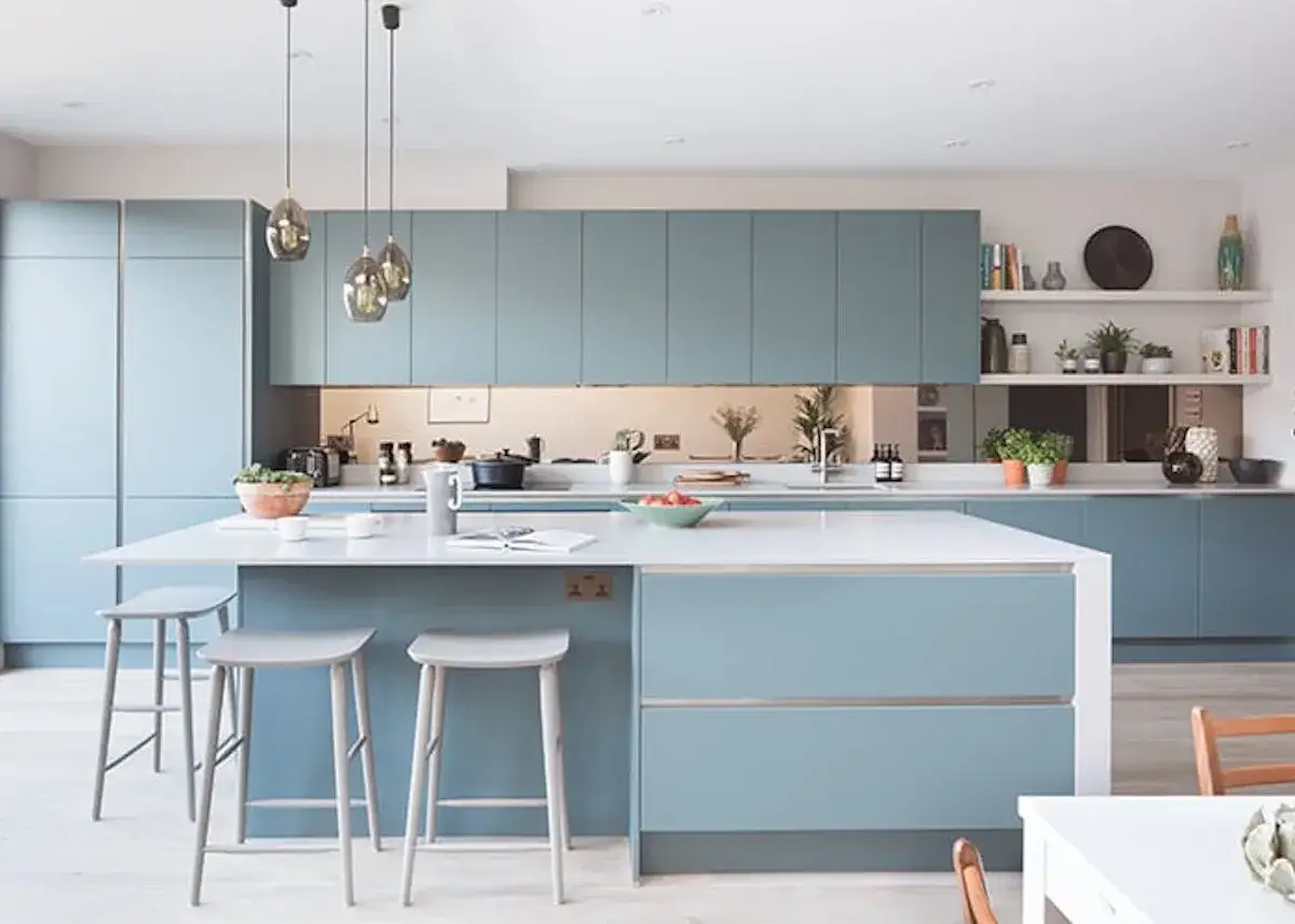 Cuisine moderne aux armoires bleu glacier, îlot central avec tabourets, et étagères décorées.