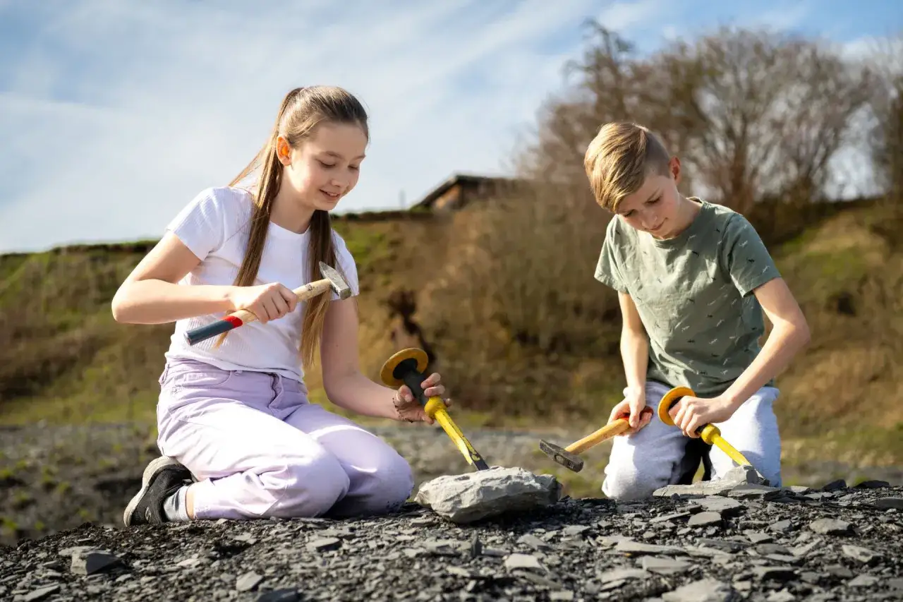 Zwei Kinder knien im Freien und graben mit Hämmern und Meißeln nach Fossilien. Vielleicht sind sie auf einer spannenden Entdeckungsreise in der Nähe von Stuttgart.