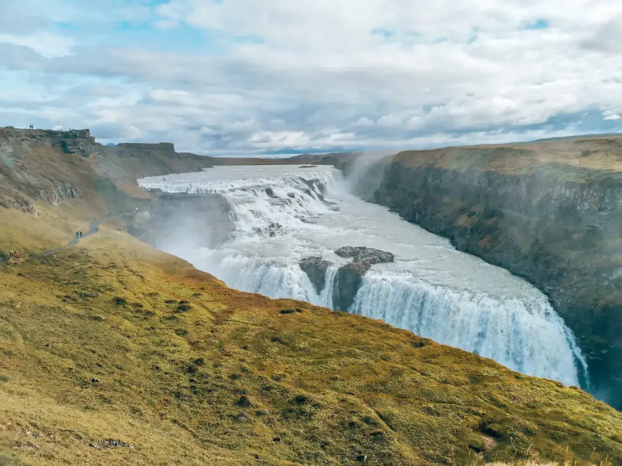 Potężny wodospad Gullfoss, cel podróży po Islandii, w otoczeniu surowego krajobrazu.