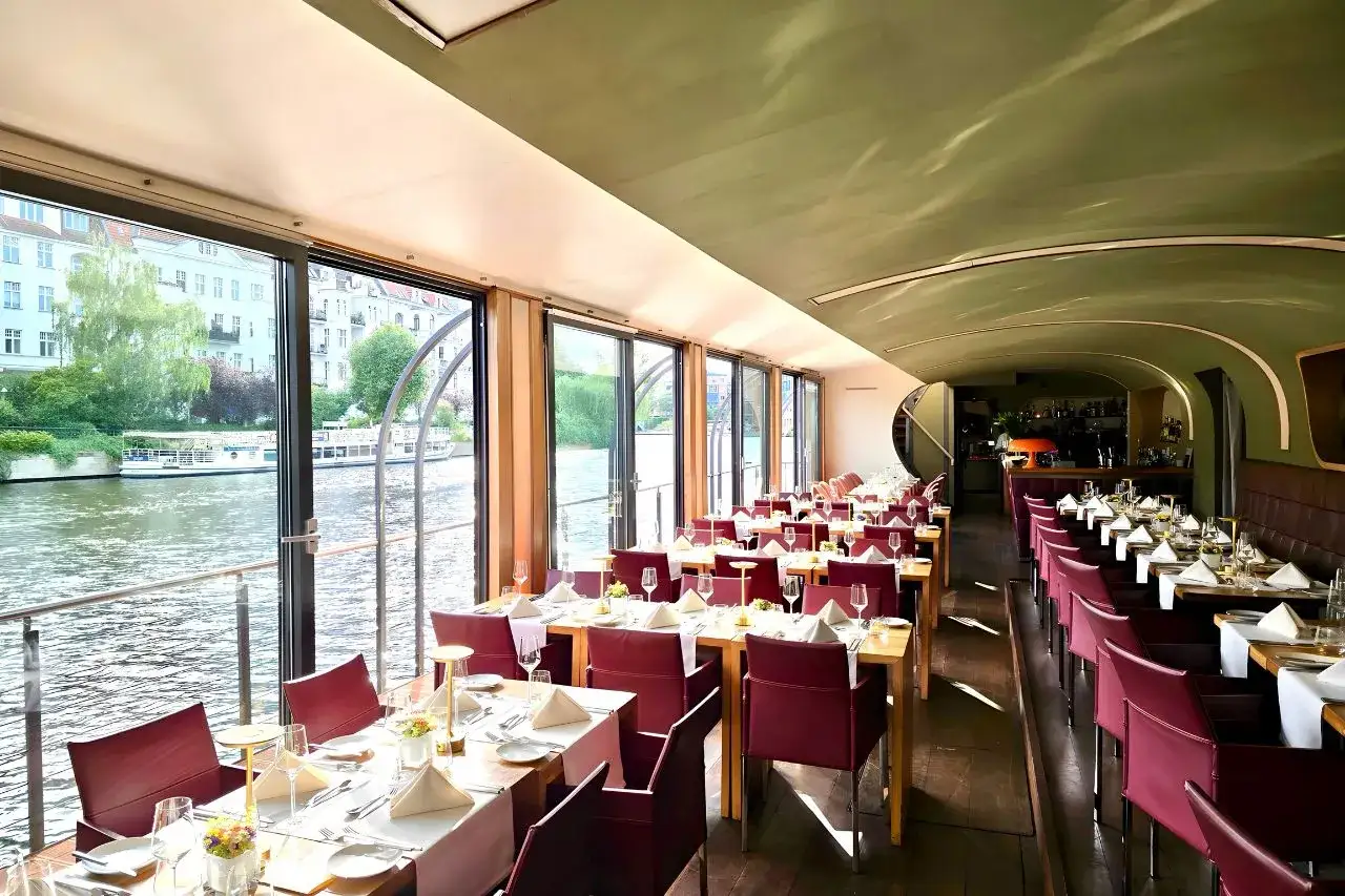 Elegantes Restaurant mit Blick auf den Fluss, eine Auswahl an besonderen Restaurants in Berlin. Tische sind für Gäste gedeckt.