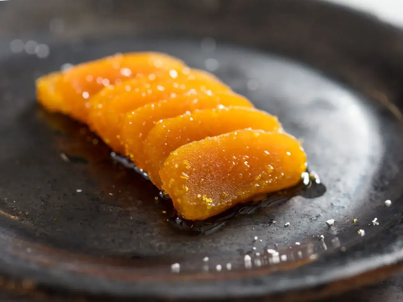 Dünne Scheiben von Bottarga di Muggine liegen auf einem dunklen Teller, glänzend und mit Salz bestreut.