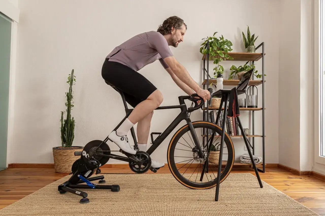 Man on a bike trainer, focused on a laptop, likely performing a 5 minute ftp test. Plants and shelves in the background.