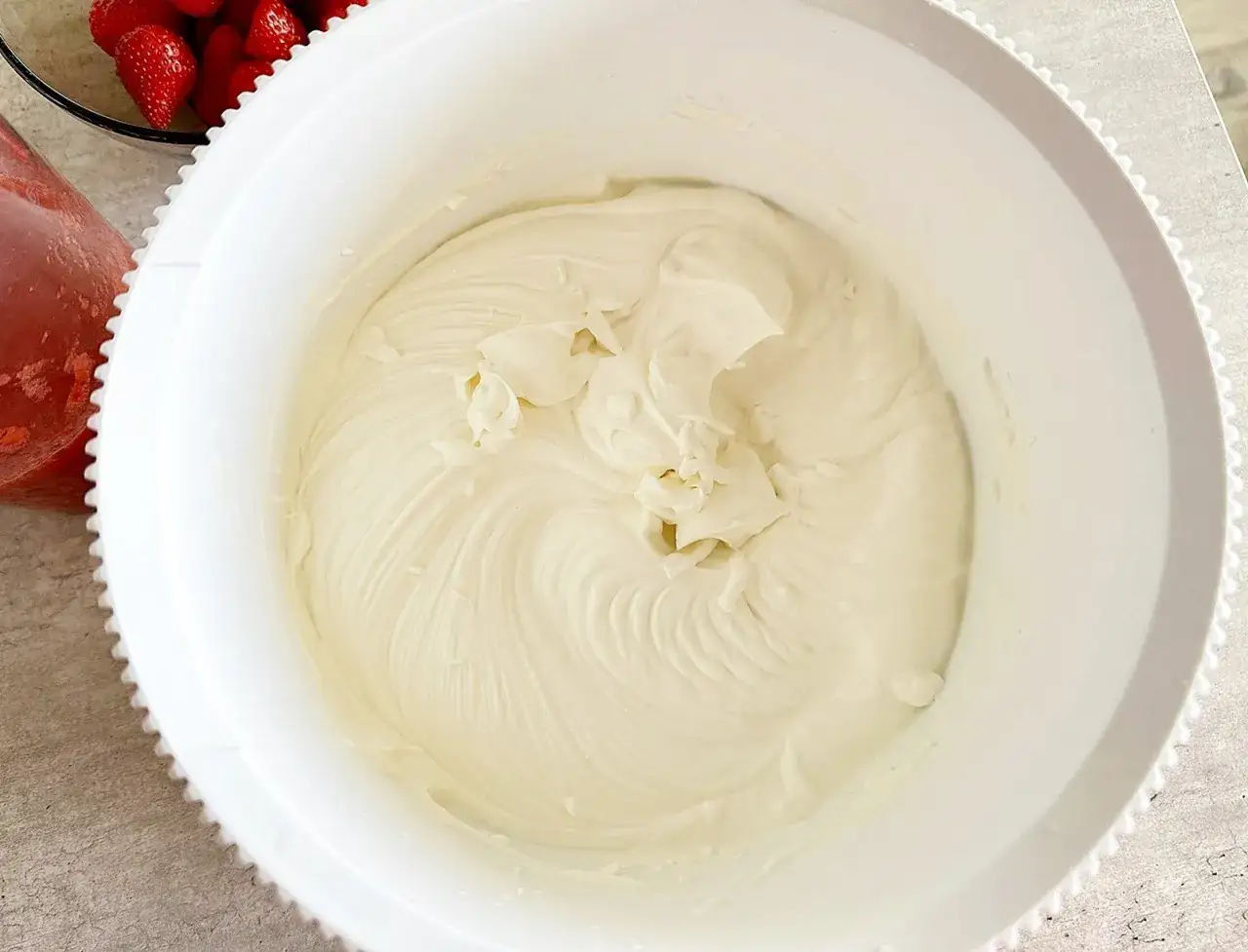 Gładki, puszysty krem z mascarpone w białej misie, gotowy do deseru. Obok miski widać miseczkę z truskawkami.