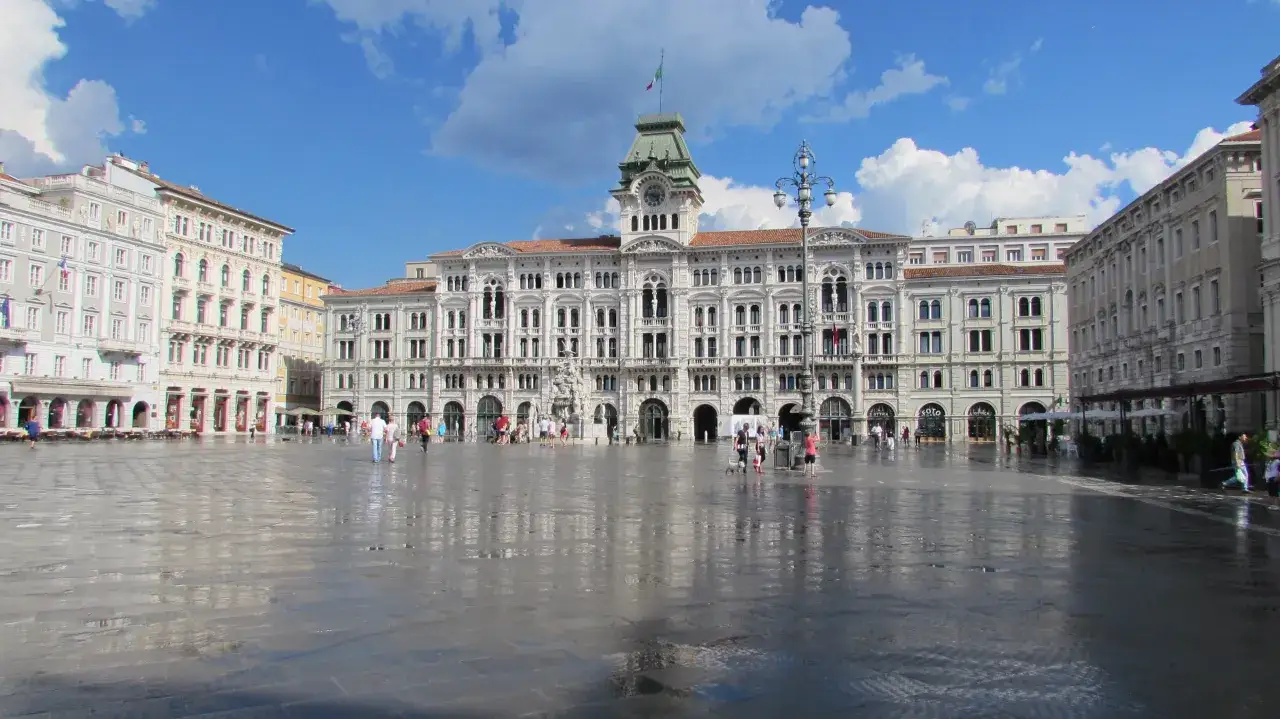 Piazza Unità d'Italia w Trieście, z pięknymi budynkami i odbijającą się w mokrym bruku architekturą. Idealne miejsce, by zacząć zwiedzanie Triestu.