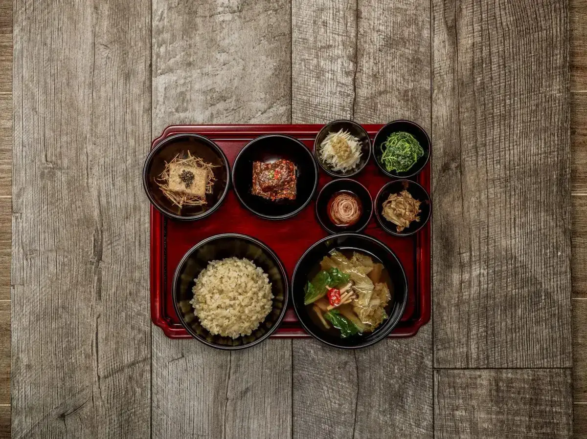 Korean temple food: eine Schale Reis, Tofu, Kimchi und verschiedene Gem&uuml;sebeilagen auf einem roten Tablett.