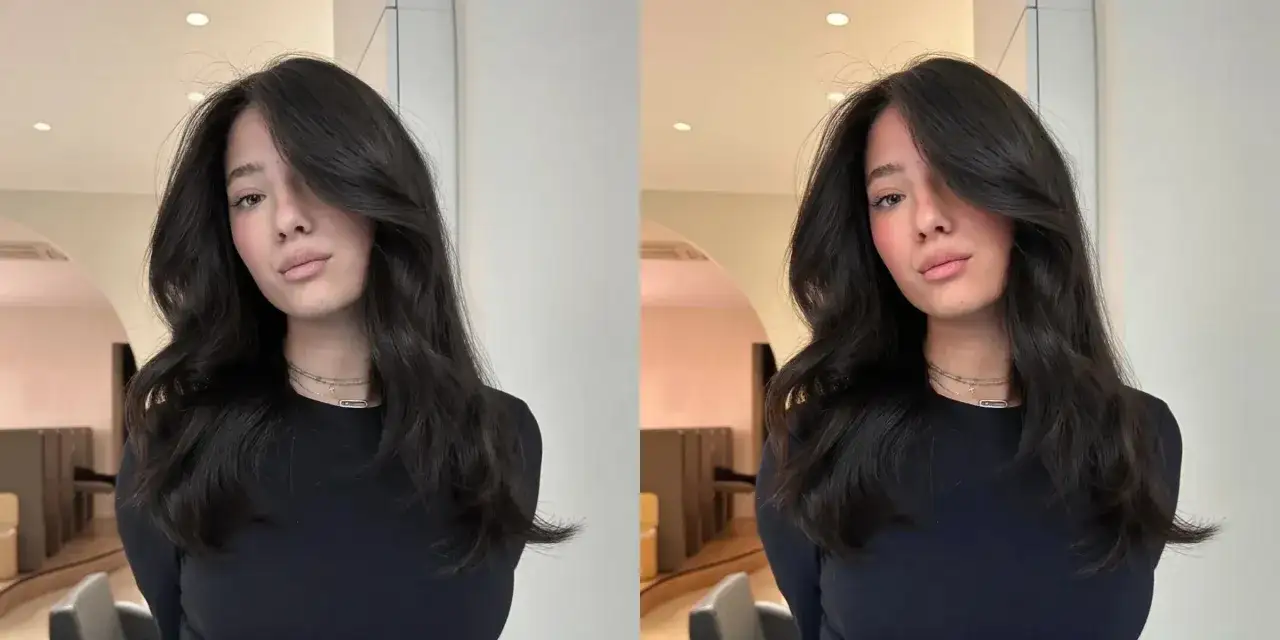 Une jeune femme aux longs cheveux bruns ondulés, mise en valeur par un subtil effet couleur cheveux, pose devant un mur clair.