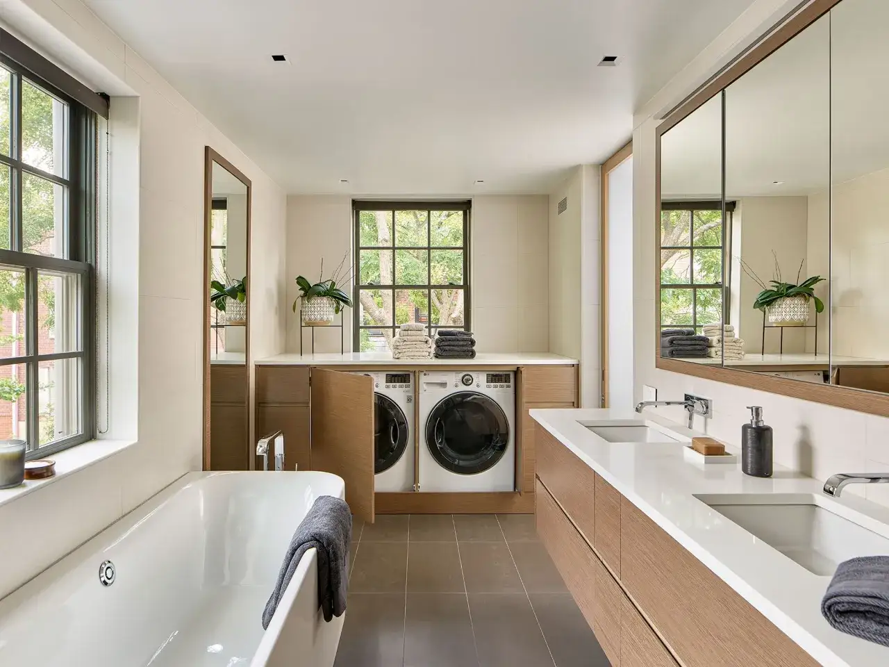 Coin buanderie dans salle de bain moderne avec baignoire, double vasque et lave-linge/s&egrave;che-linge int&eacute;gr&eacute;s dans des placards en bois.