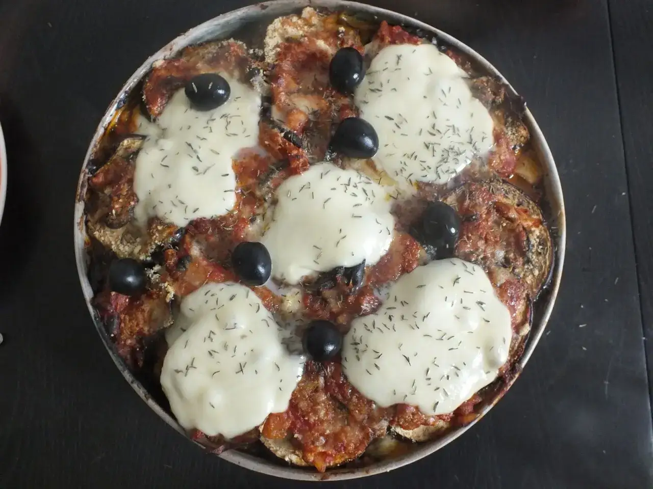 Un plat de recette aubergine mozzarella gratin&eacute;e, avec des rondelles d'aubergine, sauce tomate, mozzarella fondue et olives noires.