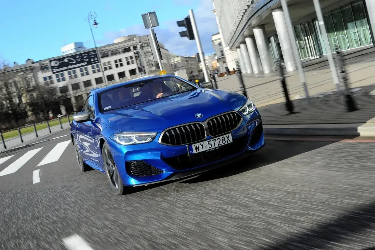 Niebieskie BMW M850i sunie po miejskiej ulicy, odbijając światło na swojej lśniącej karoserii.