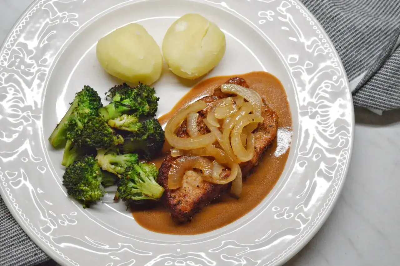 En tallrik med ugnsbakade kotletter, serverade med en kr&auml;mig s&aring;s, &aring;ngad broccoli och kokt potatis. En klassisk svensk middag.