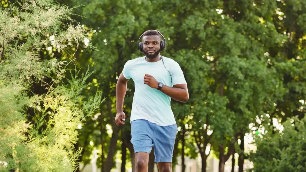 Ein Mann l&auml;uft mit Kopfh&ouml;rern durch einen Park. Er ist ein Beispiel daf&uuml;r, was 10000 Schritte am Tag bringen k&ouml;nnen: Fitness und Wohlbefinden.
