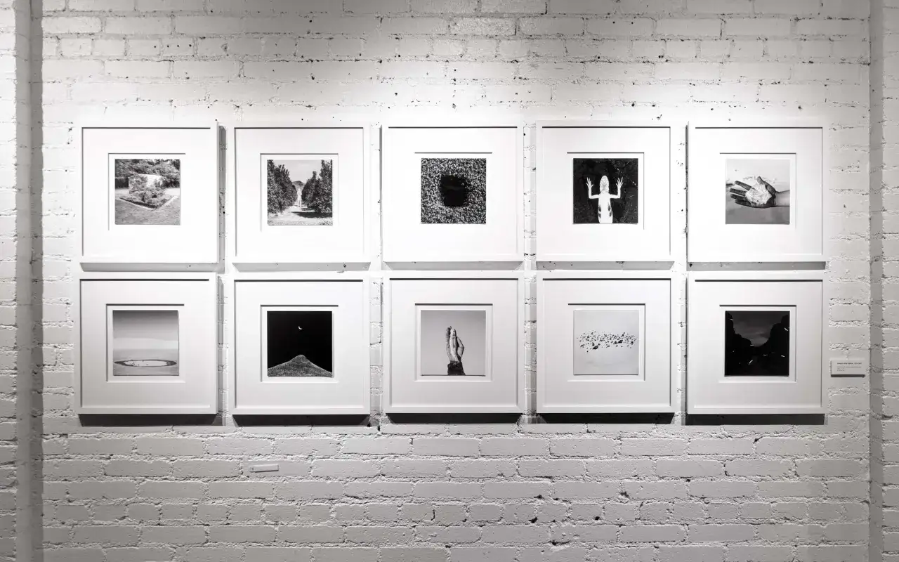 Dieci fotografie in bianco e nero, in formato dng file, esposte su una parete di mattoni bianchi.