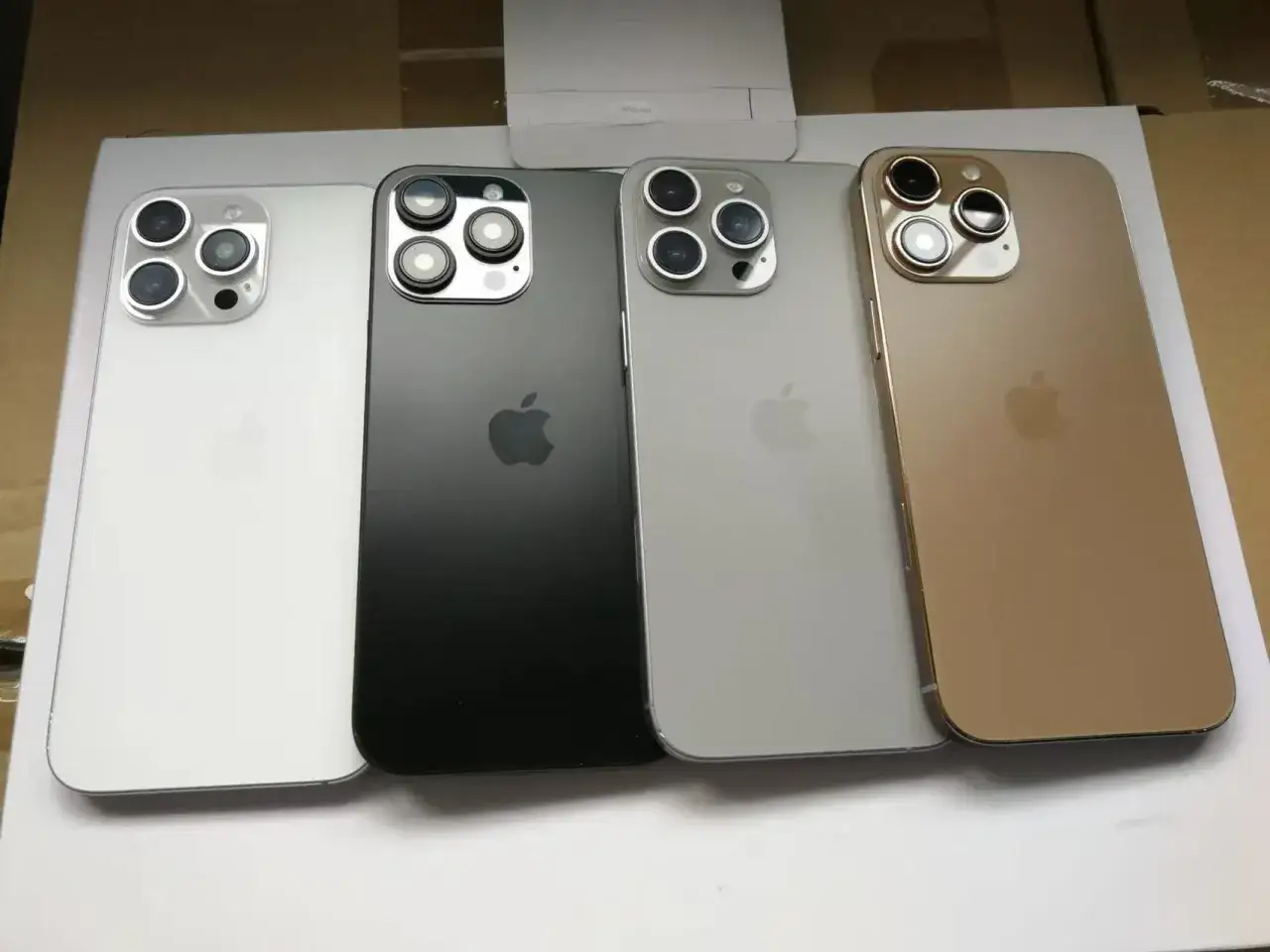 Cztery telefony iPhone 16 w kolorach białym, czarnym, srebrnym i złotym, każdy z potrójnym aparatem.