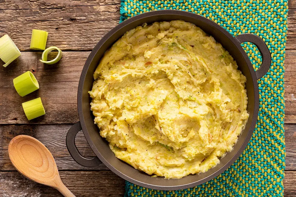 Un invitante pure di patate e porri in una padella, pronto per essere gustato. Pezzi di porro fresco decorano il tavolo di legno.