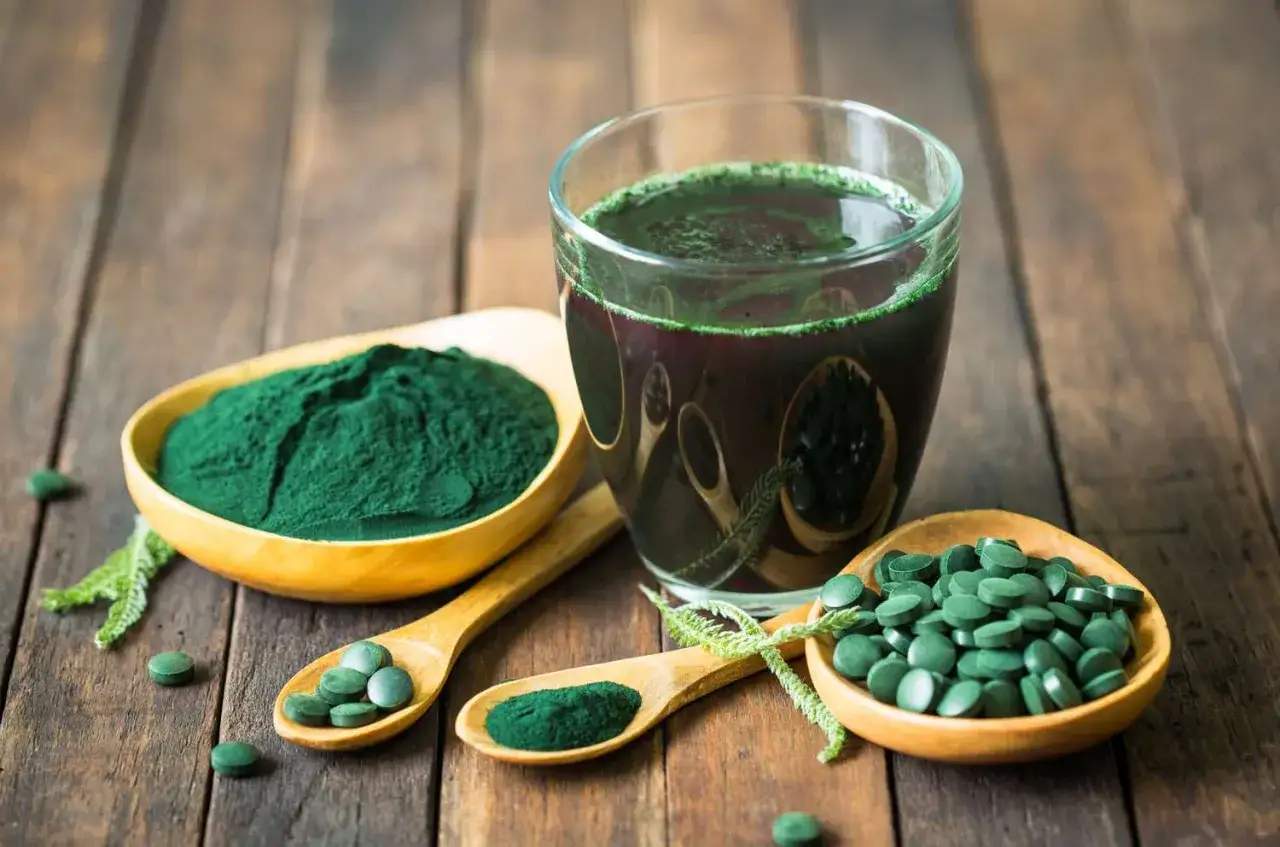 Gr&uuml;nes Spirulinapulver, Tabletten und ein Getr&auml;nk auf einem Holztisch. Was ist Spirulina? Ein Superfood f&uuml;r Energie.