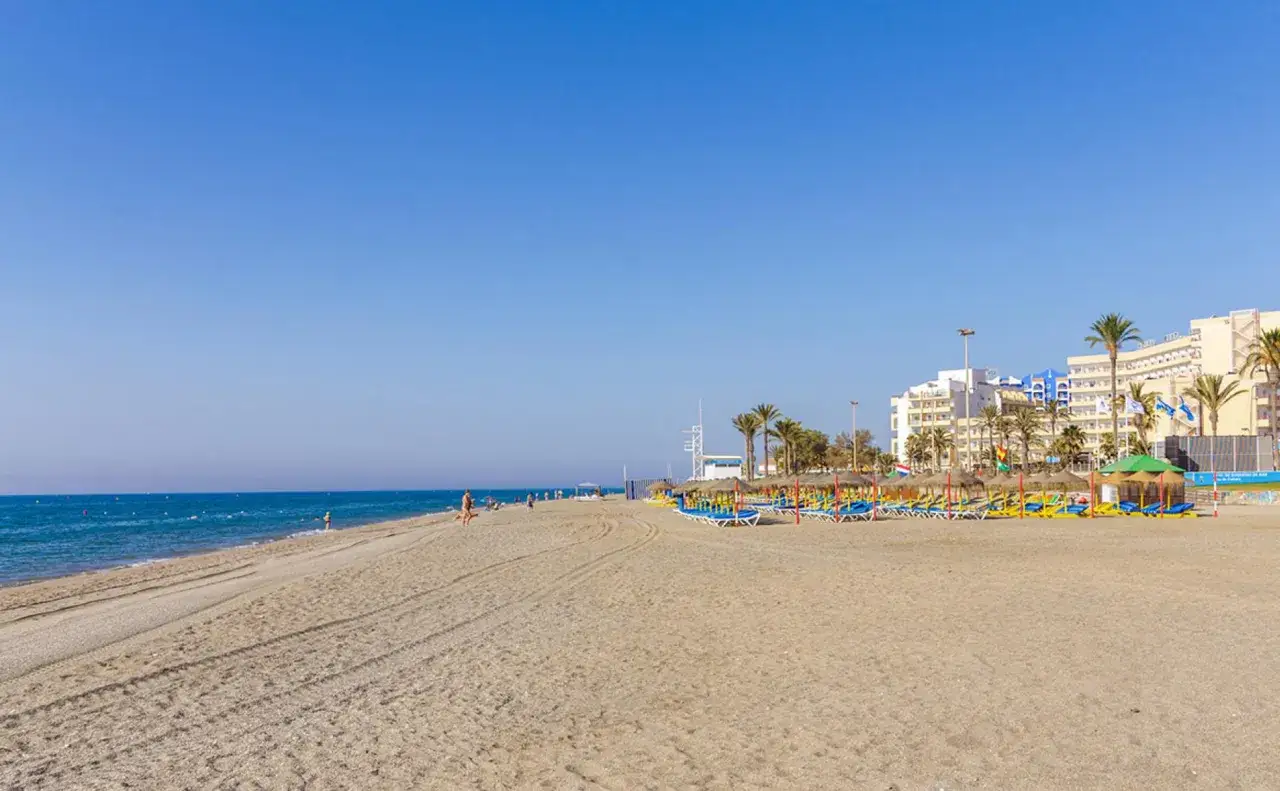 Amplia playa de la urbanización de Roquetas con sombrillas, tumbonas y hoteles al fondo.