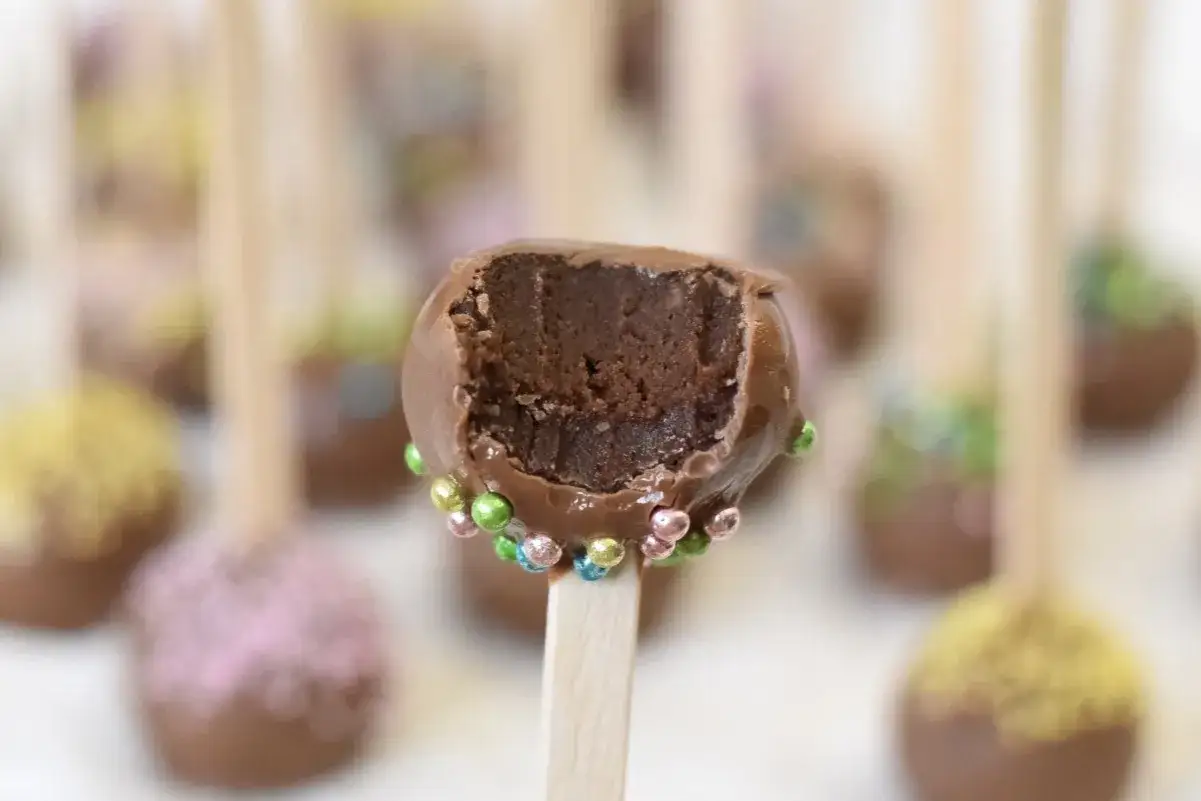 Chokladiga cake pops med färgglada strössel. En är uppäten och visar det saftiga inkråmet.