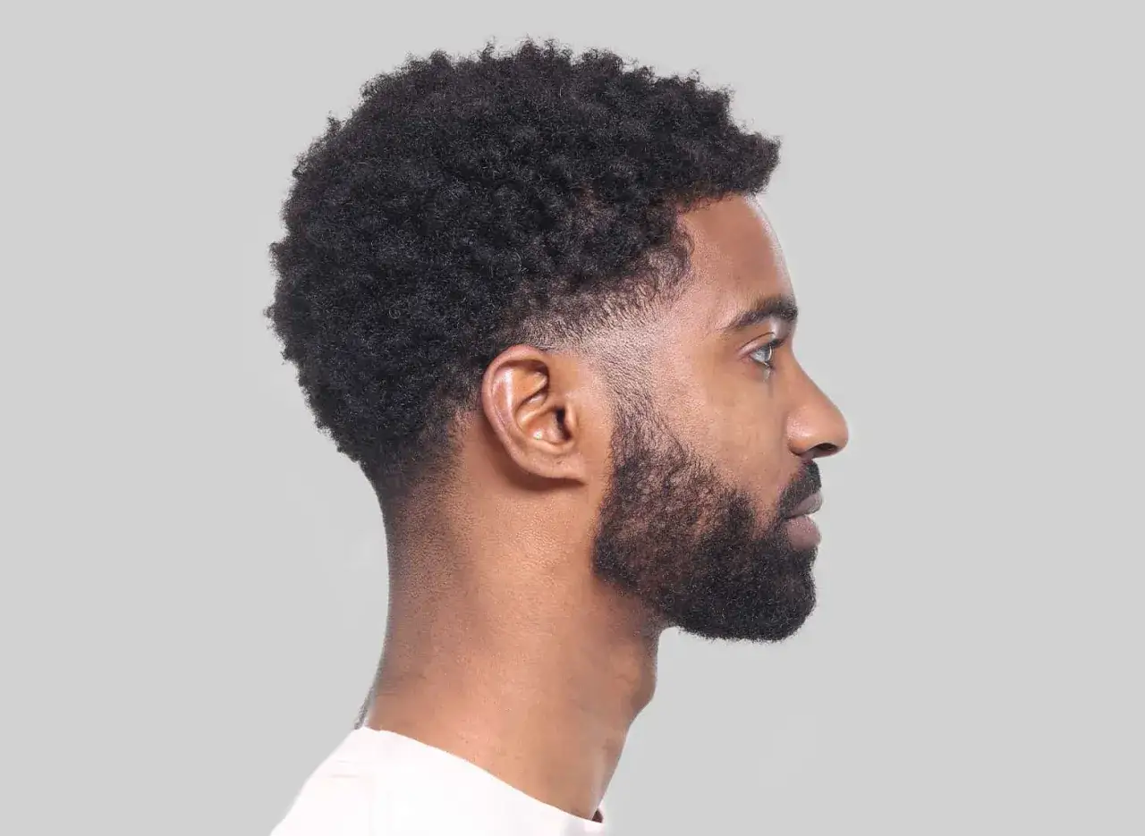 Perfil de hombre con cabello rizado y barba, luciendo un corte tuper fade impecable.
