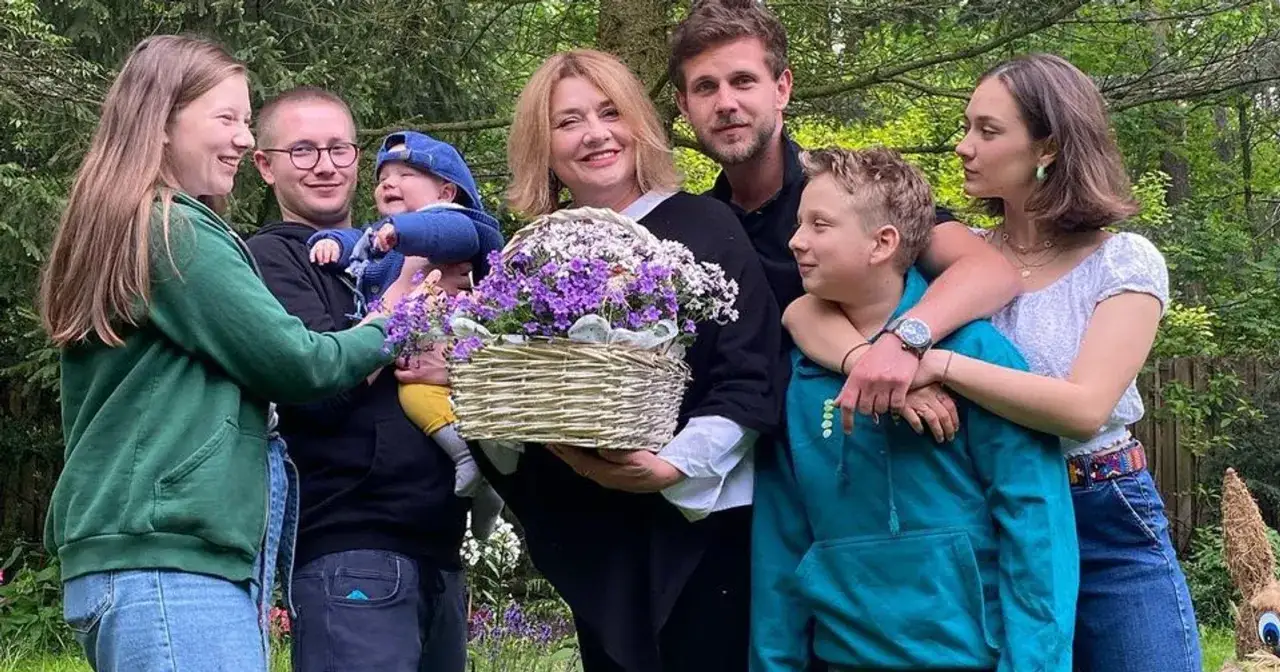 Radosna rodzina, w tym dzieci Pawła Królikowskiego, cieszy się wspólnym czasem na łonie natury, trzymając kosz kwiatów.