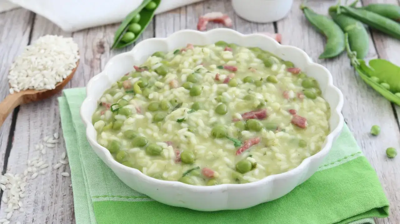 Un cremoso risotto con piselli freschi e cubetti di pancetta, servito in una ciotola bianca su un tovagliolo verde.
