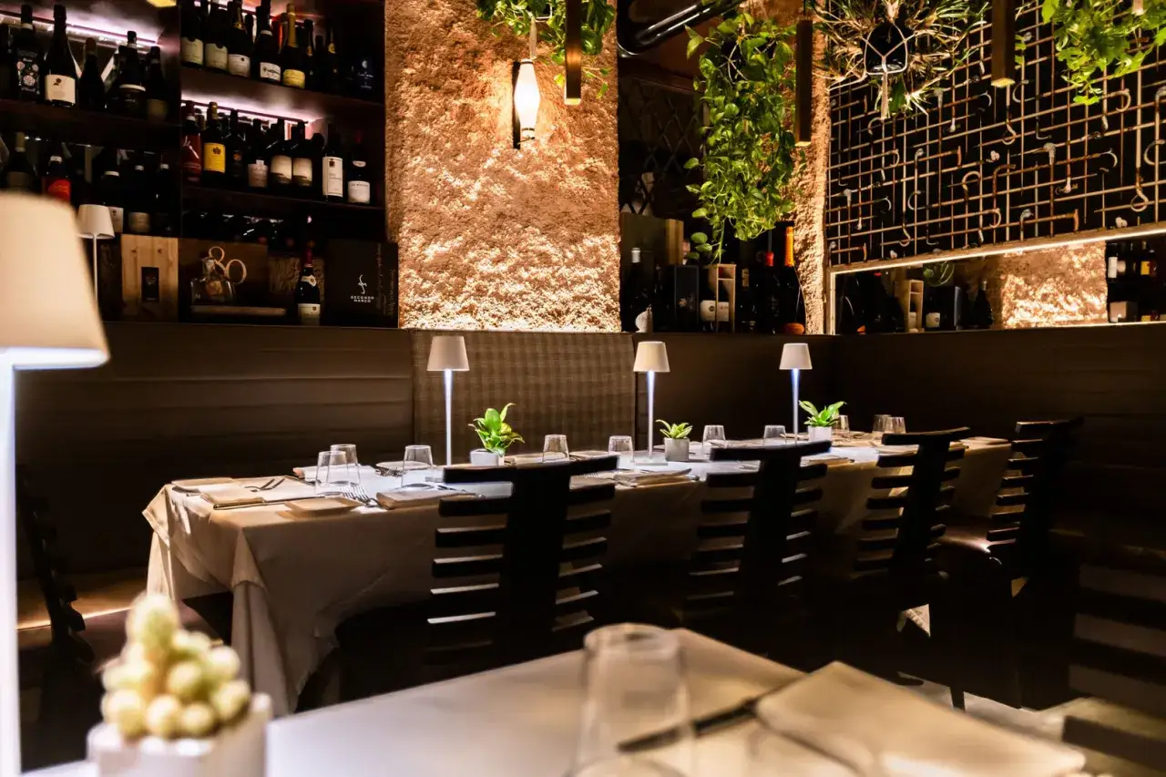 Tavoli apparecchiati in un ambiente elegante, con bottiglie di vino in bella vista. Un'atmosfera perfetta per scoprire i migliori ristoranti di Verona.